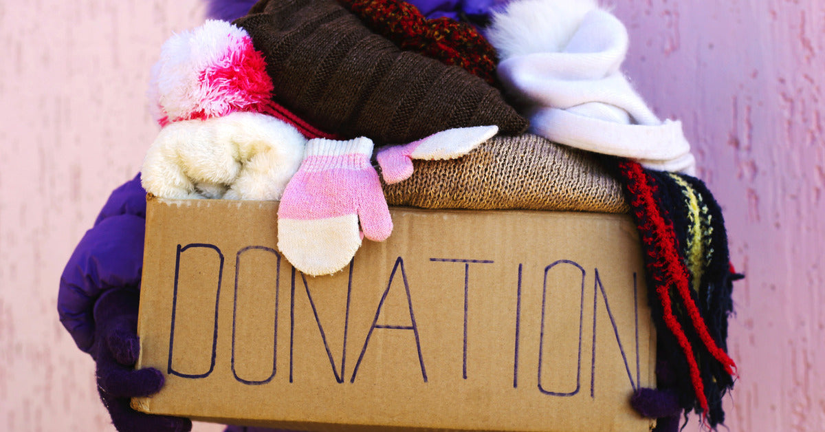 Close-up of a woman holding a donation box with winter gear. The box has hats, gloves, scarves, and other items.