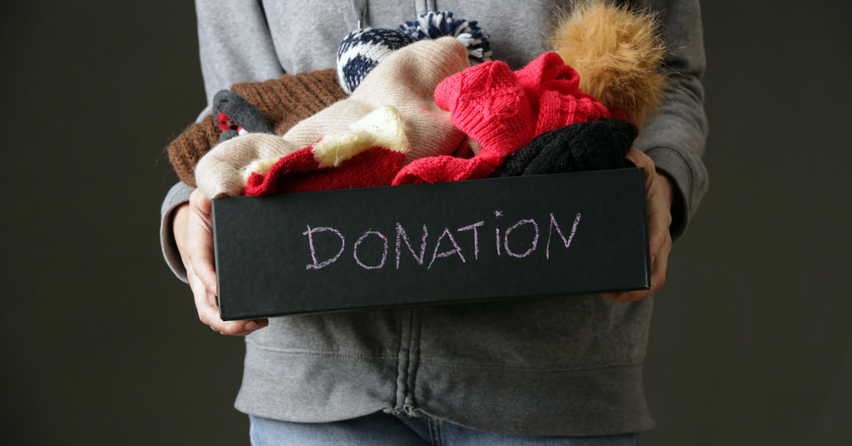 A close-up of someone holding a black box that says, "donation." The box has winter clothing like hats and gloves.